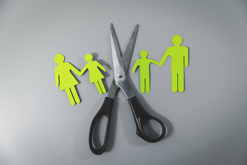 Paper cutouts of mother holding hands with child, large scissors next to paper cutouts of father holding child's hand showing child custody with separated parents.