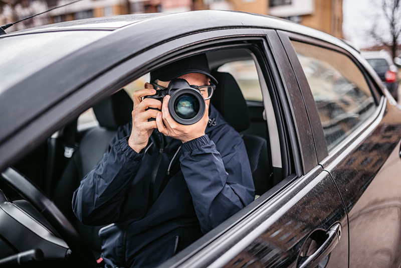 Private detective or investigator with camera taking pictures from driver's seat in car.